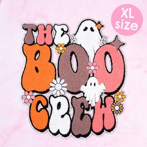 Może przedstawiać: Naszywka w rozmiarze XL z napisem "THE BOO CREW" w kolorze pomarańczowym, brązowym i różowym, z białymi postaciami duchów i kwiatami. Naszywka ma retro design ze srebrną obwódką. Idealna na Halloween.
