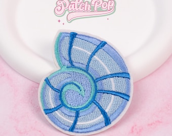May include: Embroidered patch in the shape of a nautilus shell, featuring shades of blue and teal. The patch has a white border and is set against a white background. The text "Patch Pop" is visible in the upper portion of the image.