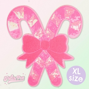 May include: A large, pink sequined candy cane patch with a matching bow. The candy cane design features alternating sections of solid pink and iridescent sequins. The patch has the text "XL size" in a purple circle.