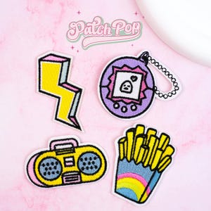 May include: Four embroidered patches with a retro theme. Includes a yellow lightning bolt, a purple handheld game, a yellow boombox, and a carton of fries with a rainbow design. The text "Patch Pop" is arched above.