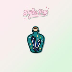 May include: A teal blue glass bottle with a cork stopper filled with blue crystals and white stars. The bottle is a patch with the text "Patch Pop" above it.