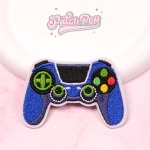 Può includere: Toppa ricamata a forma di controller di gioco blu con pulsanti neri, verdi e rossi. La toppa presenta il testo "Patch Pop" in rosa, in corsivo.