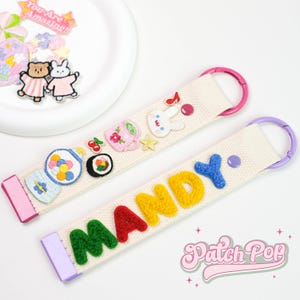 May include: Two off-white keychains with colourful patches and metal rings. One keychain spells "MANDY" in green, red, yellow, and blue letters. The other has patches of a gumball machine, sushi, and a bunny. The text "Patch Pop" is in the bottom right.