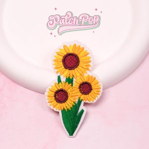 May include: Embroidered patch featuring three sunflowers with yellow petals and dark red centers, atop green leaves. The patch has a white border and the text "Patch Pop" in a cursive font.