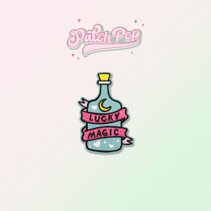 May include: A blue glass bottle with a pink ribbon and the text "Lucky Magic" on it. The bottle has a yellow cork and a crescent moon with a white heart inside.