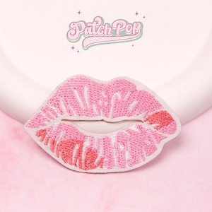 Może przedstawiać: Haftowana naszywka z różowymi ustami z białymi przeszyciami i czerwoną plamą szminki. Naszywka jest umieszczona na miękkim, różowym tle z tekstem "Patch Pop" w stylu retro.