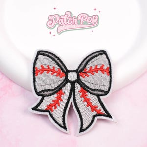Könnte beinhalten: Gestickter Aufnäher in Form einer Schleife mit Baseball-Naht-Design. Die Schleife ist grau mit roten Nähten und schwarzer Umrandung. Sie hat einen weißen Rand und den Text "Patch Pop" in rosa, kursiver Schrift.