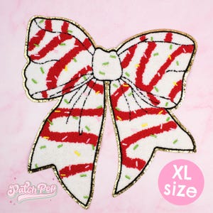 Könnte beinhalten: Ein XL-großer, weißer Aufnäher in Schleifenform mit roten Streifen und bunten Streuseln. Die Schleife hat einen goldenen Rand und befindet sich auf einem rosa Hintergrund. Der Text "XL size" befindet sich in einem rosa Kreis. Der Aufnäher ist von "Patch Pop".