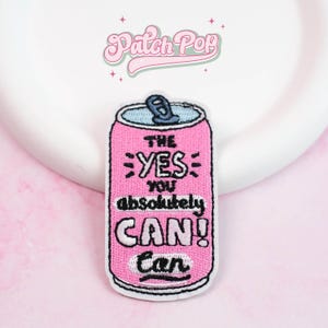 Pode incluir: Patch bordado rosa em forma de lata de refrigerante com o texto "THE YES YOU absolutely CAN! Can" em preto. A parte superior da lata é azul com uma aba prateada. O patch tem uma borda branca e a marca "Patch Pop" em rosa.