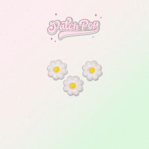 Puede incluir: Tres parches de hierro de margarita blanca con centros amarillos. Los parches están dispuestos en forma triangular sobre un fondo blanco.