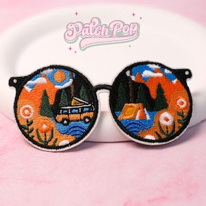 May include: Embroidered patch shaped like sunglasses, depicting a camping scene with a van, tent, and mountains. The patch has a black frame and a white border. The text "Patch Pop" is arched above the sunglasses.