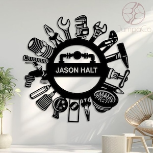 May include: Black metal wall art featuring a circular design with various plumbing tools arranged around a central section. The text "JASON HALT" is displayed in the center. The design includes wrenches, pliers, and other tools.