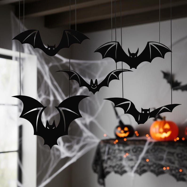 Pu&ograve; includere: Decorazioni a forma di pipistrello nero appese al soffitto. I pipistrelli hanno ali dettagliate e sono sospesi con fili sottili. Lo sfondo include una finestra, ragnatele e un tavolo con zucche illuminate, creando un tema di Halloween.