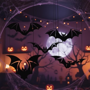 Pu&ograve; includere: Decorazioni a forma di pipistrello nero appese al soffitto, a tema Halloween. I pipistrelli sono sagomati su uno sfondo viola con una luna piena, ragnatele e zucche. I pipistrelli sono sospesi da sottili fili neri.