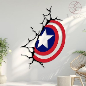 Op de afbeelding: Een muursticker met Captain America's schild, met een witte ster op een blauwe cirkel, omringd door rode en witte ringen. Het schild lijkt door een muur te breken, met zwarte scheurlijnen die naar buiten uitstralen.