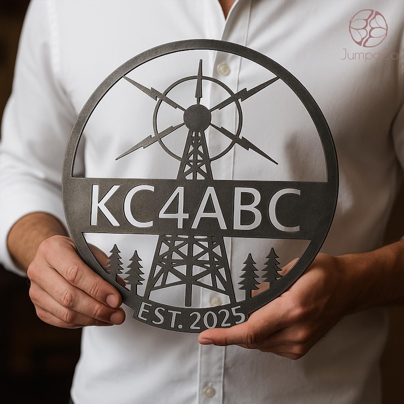 May include: A circular, dark metal sign featuring a radio tower design with the text "KC4ABC" and "EST. 2025". The sign includes a stylized antenna and pine trees, suitable for home decor or a gift.