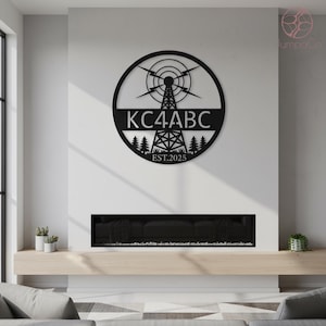 May include: Black metal wall art featuring a radio tower design within a circle. The text "KC4ABC" is displayed prominently, with "EST.2025" below. The artwork includes stylized trees and lightning bolts, suitable for home decor.