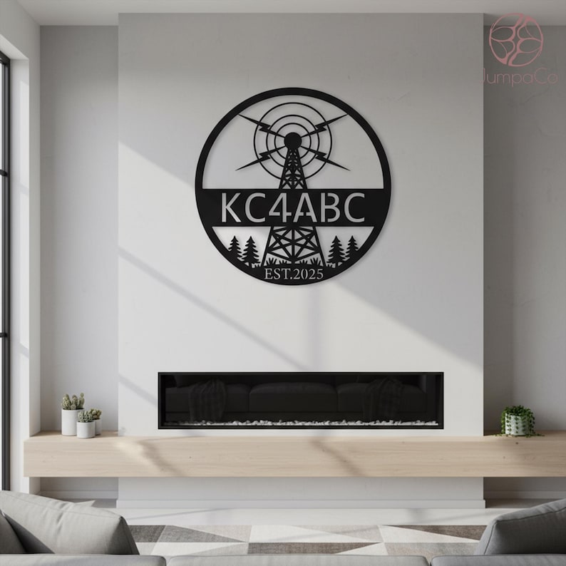 May include: Black metal wall art featuring a radio tower design within a circle. The text "KC4ABC" is displayed prominently, with "EST.2025" below. The artwork includes stylized trees and lightning bolts, suitable for home decor.