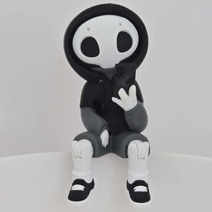 Könnte beinhalten: Figur einer Skelettfigur mit schwarzem Kapuzenpullover und grauer Hose, die ein Smartphone hält. Das Skelett hat einen weißen Schädel mit großen schwarzen Augenhöhlen und trägt schwarz-weiße Schuhe. Die Figur sitzt.