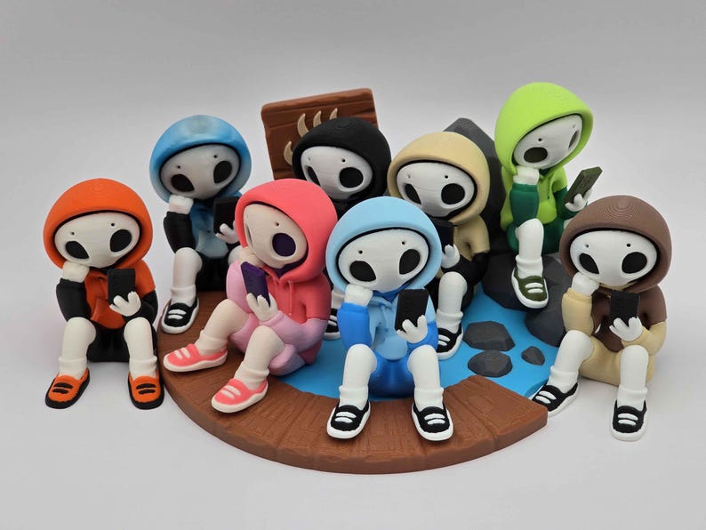 May include: A group of stylized figurines, each wearing a different colored hoodie and holding a smartphone. The figures are seated on a circular platform with a blue and brown design, suggesting a social gathering or digital interaction theme.