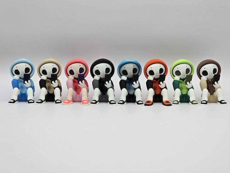 May include: A row of eight colorful figurines, each depicting a skeleton-like character in a hoodie, seated and holding a smartphone. The figurines are in various colors, including blue, tan, pink, black, and green, with black shoes.