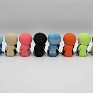 May include: A row of eight small, seated figurines in various colors: light blue, beige, pink, black, blue-white gradient, orange, green, and brown. Each figurine is seated with its back facing the viewer, with black and white shoes.
