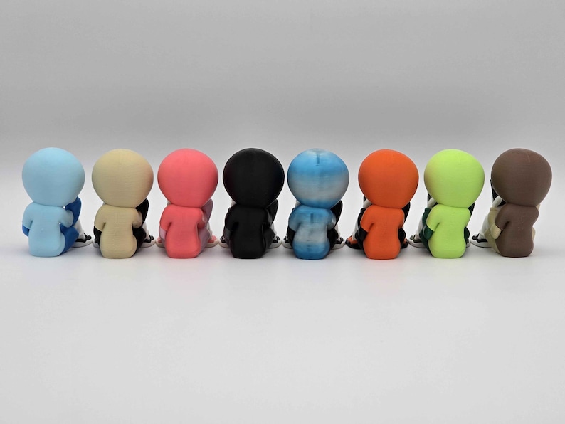 May include: A row of eight small, seated figurines in various colors: light blue, beige, pink, black, blue-white gradient, orange, green, and brown. Each figurine is seated with its back facing the viewer, with black and white shoes.