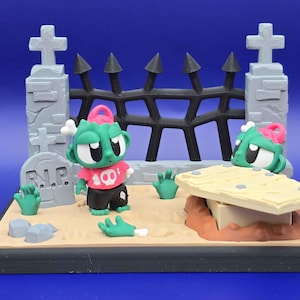 May include: A miniature zombie-themed diorama featuring a graveyard scene. The scene includes a tombstone, a coffin, a fence, and several zombie figures with green skin, pink brains, and bone accents. The zombies wear red shirts and black shorts.