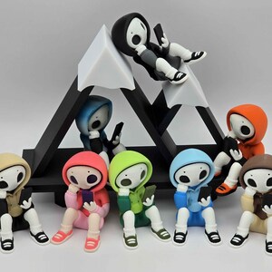 May include: A collection of colorful figurines, each depicting a figure in a hoodie, holding a smartphone. The figures are arranged around a black and white geometric structure resembling a mountain. The hoodies are in various colors, including red, blue, and green.