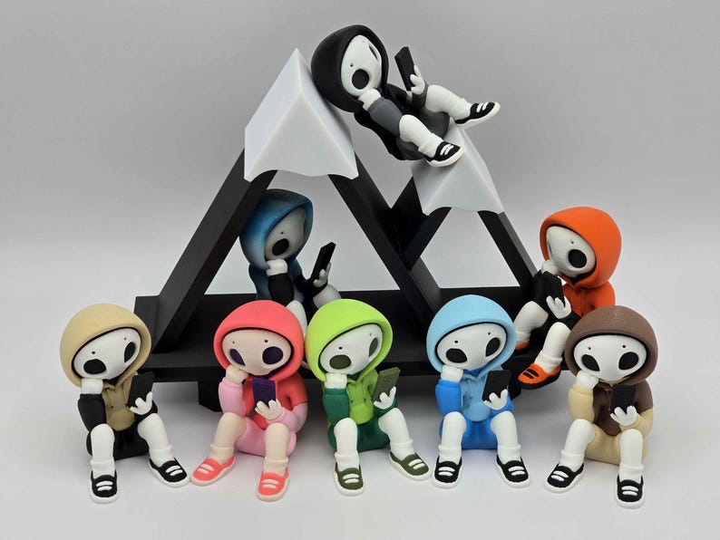 May include: A collection of colorful figurines, each depicting a figure in a hoodie, holding a smartphone. The figures are arranged around a black and white geometric structure resembling a mountain. The hoodies are in various colors, including red, blue, and green.