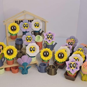 May include: A collection of 3D printed flower pot figurines with smiling faces and numbers on them. The figurines are arranged on a wooden stand with a sign that reads "BLOOM PLANT".