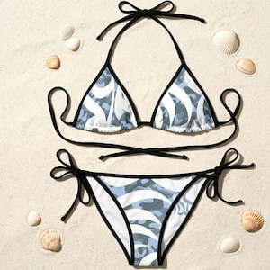 May include: A two-piece bikini set featuring a light blue and white abstract wave pattern. The top is a triangle style with black trim and thin black tie straps. The matching bottom has side tie closures and black trim along the edges.