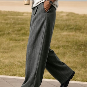 May include: Wide-leg trousers in a dark charcoal grey fabric featuring a subtle vertical pinstripe pattern. These full-length trousers have a tailored fit with side pockets and a clean, straight-leg silhouette that falls to the ankles.