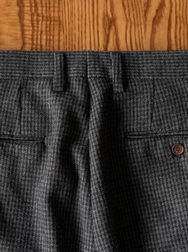 K&ouml;nnte beinhalten: Nahaufnahme der R&uuml;ckseite einer Hose mit grauem und schwarzem Muster. Die Hose hat zwei Ges&auml;&szlig;taschen, G&uuml;rtelschlaufen und einen Knopfverschluss. Der Stoff hat ein subtiles strukturiertes Aussehen.