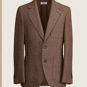 Op de afbeelding: Een bruine blazer met visgraatmotief, voorzien van een ingekeepte revers, twee donkere knopen, twee grote opgestikte zakken op de taille en een opgestikte borstzak. Het label in de binnenkraag bevat de tekst "Vintage" in een schrijfletter.