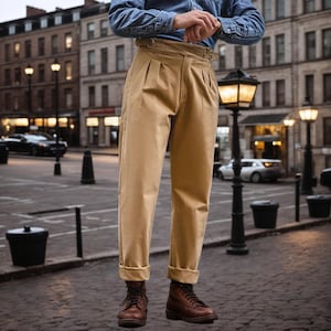 Puede incluir: Pantalones color caqui de talle alto con una correa de ajuste con hebilla lateral en la cintura, doble pliegue en la parte delantera y dobladillos con vuelta. Los pantalones se combinan con una camisa azul y botas de cuero marr&oacute;n.