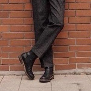 May include: A pair of dark charcoal gray trousers with a subtle textured pattern paired with black leather ankle boots. The trousers feature a straight-leg cut that falls to the ankle, while the boots have a smooth finish and a low heel.