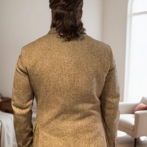 May include: A tan herringbone blazer with a classic design. The jacket has a two-button closure and a notched lapel. The fabric has a subtle pattern and a tailored fit. The person is facing away from the camera.
