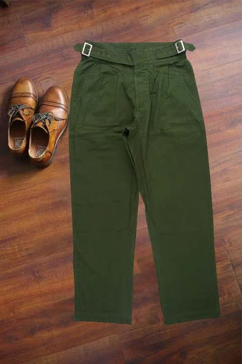 Puede incluir: Pantalones de color verde oliva con dise&ntilde;o de cintura alta, ajustadores de hebilla laterales en la pretina y un par de zapatos oxford de cuero marr&oacute;n con cordones, presentados juntos como un conjunto coordinado de ropa y calzado.
