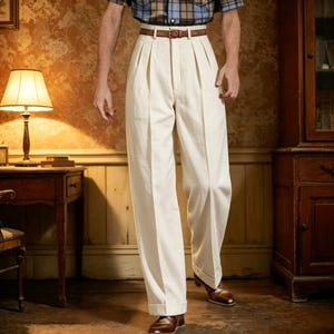 Puede incluir: Pantalones de tiro alto en color blanco roto con doble pinza frontal, corte recto y bajos con vuelta. Los pantalones se sujetan con un cinturón de cuero marrón con hebilla plateada, combinados con una camisa de cuadros metida por dentro.