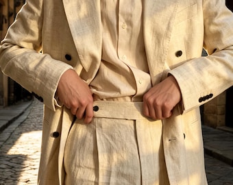 May include: A beige double-breasted blazer with dark buttons, a matching button-down shirt, and high-waisted trousers with a wide waistband. The ensemble is crafted from a textured fabric, featuring wide lapels and a structured, tailored fit.