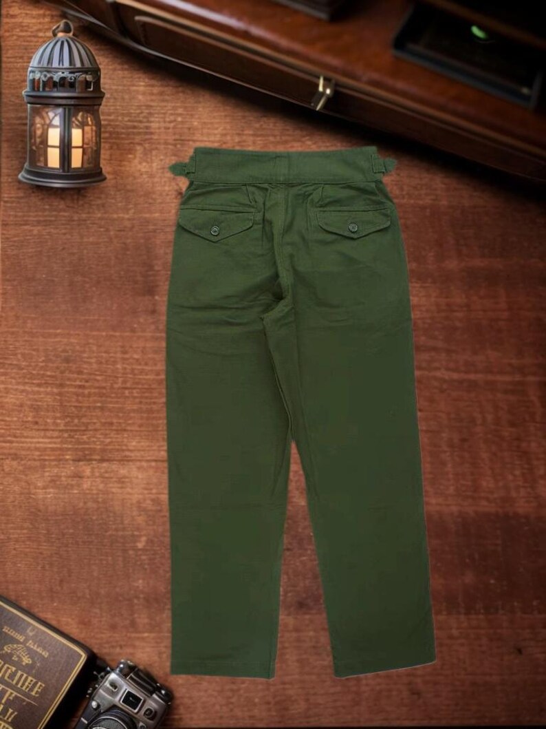 Puede incluir: Pantalones de color verde oliva con dise&ntilde;o de cintura alta, pesta&ntilde;as de ajuste laterales, dos bolsillos traseros con solapas abotonadas y corte de pierna recta. Los pantalones presentan una cinturilla estructurada y costuras visibles.