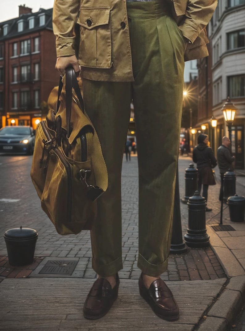 Puede incluir: Una chaqueta utilitaria color canela, pantalones plisados verde oliva con dobladillos y mocasines de cuero marr&oacute;n oscuro. Se sostiene un bolso grande de lona color canela con asas y adornos de cuero marr&oacute;n oscuro. Atuendo de corte estructurado.