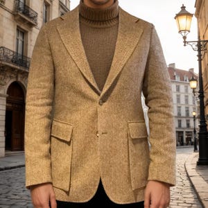 May include: A tan herringbone blazer with two front pockets and a single-button closure. The blazer is paired with a brown turtleneck sweater. The background features a European street scene with buildings and streetlights.