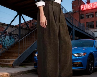 May include: High-waisted, wide-leg trousers in a dark olive-brown textured fabric. The pants feature a structured waistband with a front fly closure and subtle pleating at the hips, falling into a loose, straight silhouette that reaches the floor.