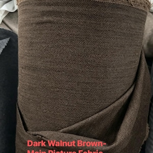 May include: A roll of dark walnut brown fabric featuring a woven herringbone pattern. The textile has a visible frayed edge at the top and a weight of about 450gsm as indicated by the text printed on the lower portion of the fabric roll.