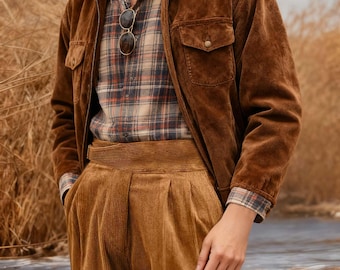May include: A brown suede jacket with two front pockets, worn over a plaid shirt and paired with corduroy pants. Sunglasses hang from the shirt. The outfit is in shades of brown and tan.