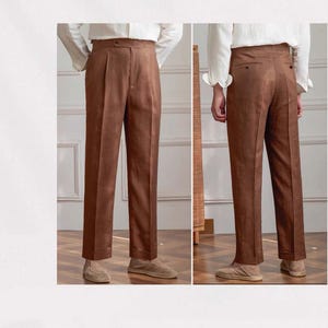 Pu&ograve; includere: Pantaloni in lino marrone a vita alta e pieghe. I pantaloni hanno una chiusura con bottoni e tasche. I pantaloni sono mostrati davanti e dietro, mettendo in risalto la vestibilit&agrave; sartoriale e il design classico. La modella indossa una camicia bianca e scarpe marroni.