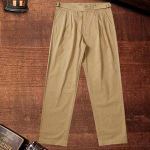 Puede incluir: Pantalones de color beige con dise&ntilde;o de cintura alta y cintur&oacute;n ajustable integrado en la pretina. Estos pantalones presentan un corte de pierna recta, cierre de cremallera frontal y pliegues sutiles bajo la cintura, ofreciendo un aspecto estructurado.