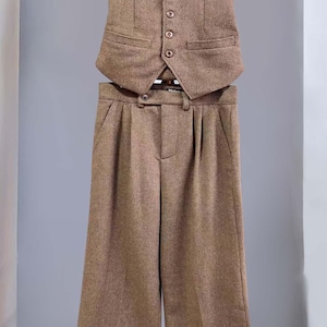 Peut inclure: Un ensemble gilet et pantalon marron à motif chevrons. Le gilet présente un col en V, cinq boutons sur le devant et deux poches passepoilées. Le pantalon a un devant plissé, une taille boutonnée et des jambes larges avec des ourlets. Une étiquette Vintage est visible.